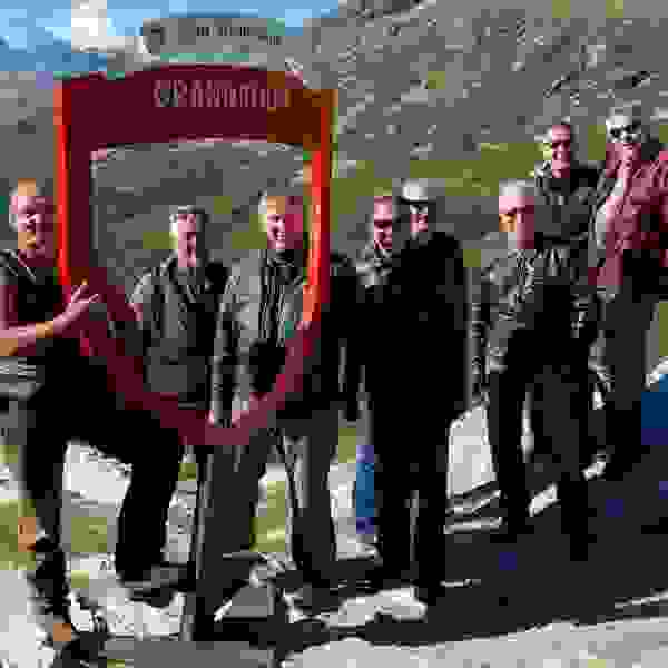 Gruppenfoto vor einem Grand Tour of Sitzerlwand Foto-Spot mit mehreren Männern in Sonnenbrille und Motorrad-Outfit.