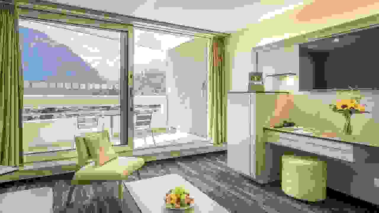 Hotelzimmer von Hotel Metropole Interlaken. Im Vordergrund ist ein Tisch mit einer Früchteschale zu sehen, im Hintergrund ein Balkon mit Blick auf die Jungfrau.