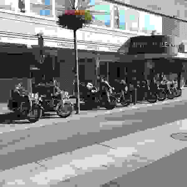 Mehrere Motorräder sind hintereinander vor einem Hotel parkiert.