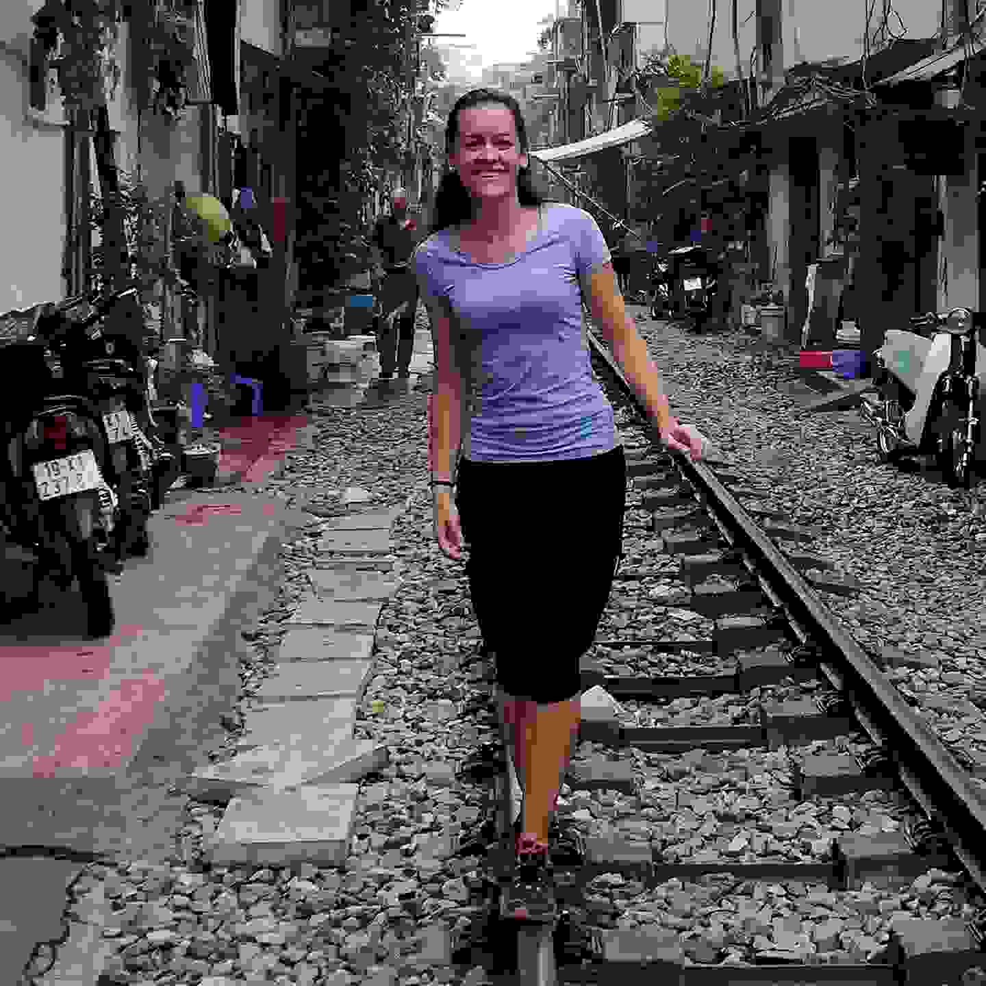 Junge Frau lacht in Kamera und läuft auf den Geleisen durch eine Strasse in Vietnam. Auslandsseminar der TFBO nach Vietnam.