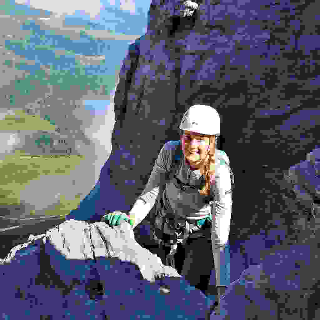 Junge Hüttenwartin, Melanie Lehnherr, ist mit einer Kletterausrüstung zu sehen. Sie befindet sich im Felsen und wird von der Sonne beleuchtet.