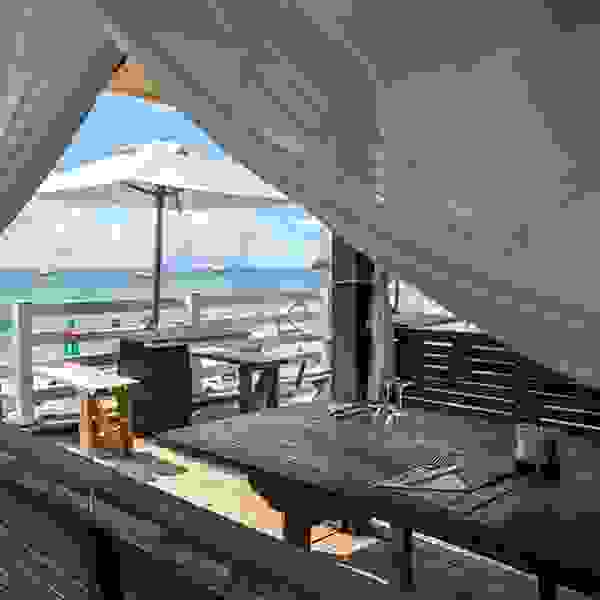Stimmungsbild von einem Restaurant mit Ausblick auf den Strand mit Sonnenschirm.